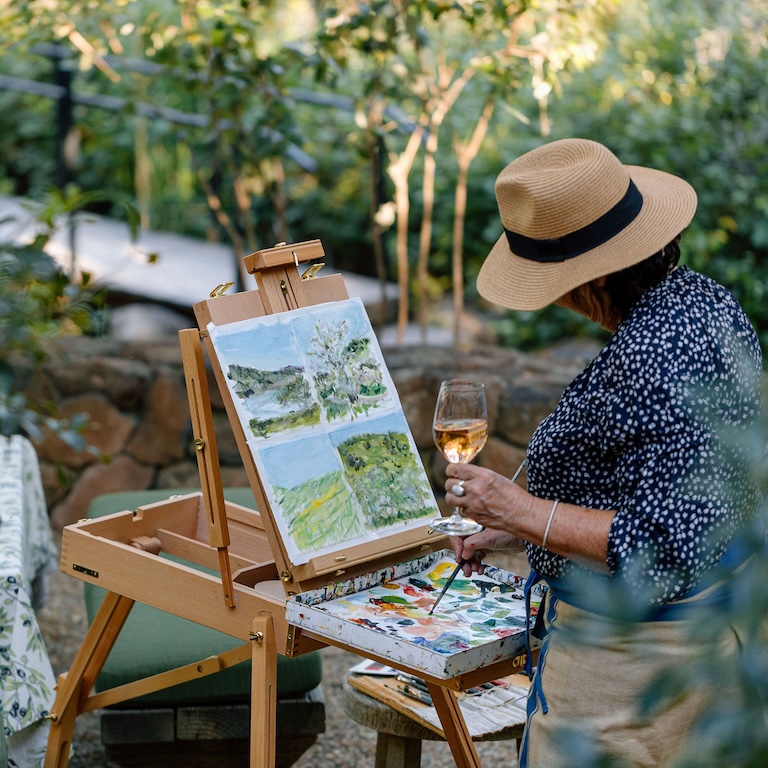 Woman painting picture while drinking glass of wine